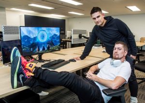 two men sitting in an office with a computer and a man with his foot on the desk